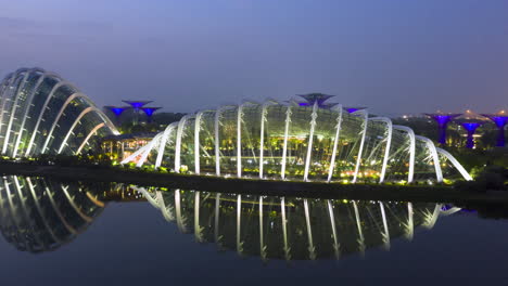 Desde-La-Noche-De-Singapur-Hasta-La-Madrugada,-El-Dron-Hiperlapso-Se-Mueve-De-Izquierda-A-Derecha-Sobre-El-Agua-Con-Jardines-Junto-A-La-Bahía,-Marina-Bay-Sands,-Súper-árboles,-Cúpula-De-Nubes,-Cúpula-De-Flores-Con-Reflejo-De-Espejo.