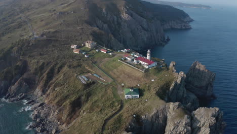 Slow-aerial-tilt-up-and-push-back-shot-of-Gamov-lighthouse-building-complex,-standing-on-steep-rocky-cliff,-on-the-sunset