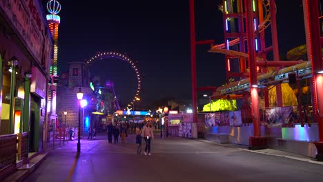 Bunter-Vergnügungspark-Mit-Riesigem-Riesenrad-Und-Menschen,-Die-Abends-Im-Wiener-Prater-Spazieren-Gehen---Weitwinkelaufnahme-4k