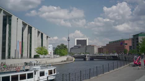 Locked-shot-of-River-Spee-with-pedestrians-using-the-bank-and-tour-boats-moving-past-in-the-water