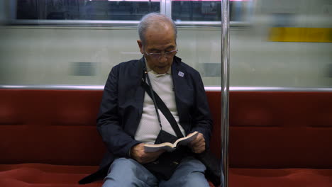 Ein-Japanischer-Alter-Mann,-Der-In-Einer-U-Bahn-Aufmerksam-Ein-Buch-Liest