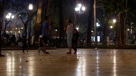 Traditional-family-with-three-kids-two-boys-and-one-girl-having-a-nice-time-at-a-local-park-at-night,-locked-low-angle-shot