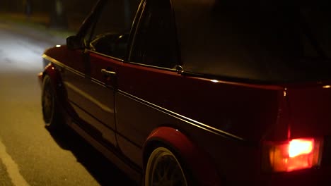 Red-modified-VW-Volkswagen-Golf-MK1-car-driving-slowly-through-city-at-night,-medium-shot