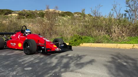 Coche-De-Carreras-Rojo-Pasando-Lentamente-En-Una-Prueba-De-Manejo-En-La-Colina-En-Imtahleb-Malta---Plano-Medio