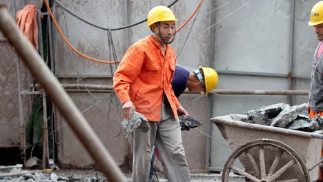 Un-Trabajador-De-La-Construcción-Carga-Escombros-Mientras-Derriban-Piso-De-Concreto-En-Un-Sitio-Usando-Un-Martillo-De-Demolición-Y-Una-Carretilla,-Un-Trabajador-De-Cámara-Lenta-Mira-En-Dirección-A-La-Cámara