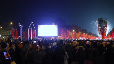 Fuegos-Artificiales-Durante-La-Llegada-De-Los-Principales-Campos-Elíseos-De-París,-Rodeados-Por-Una-Multitud-De-Personas-En-La-Calle-Principal-Con-Vistas-Al-Arco-Triunfal-Y-A-Una-Calle-Cubierta-De-Rojo.