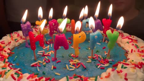 Bunte-Happy-Birthday-Kerzen-Leuchten-Auf-Einem-Bunten-Kuchen-Mit-Blauem-Zuckerguss-Und-Regenbogenstreuseln