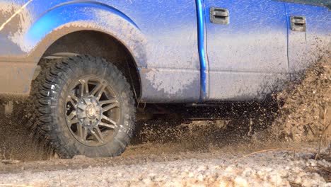 Blue-Ford-F-150-driving-along-a-mudyy-trail-and-splashing-mud,-water-and-snow-in-slow-motion