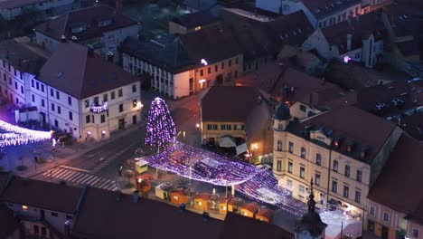 Christmas-fair-with-decoration-and-bright-lights-on-main-square-of-small-town-in-Europe,-aerial-view-of-old-medieval-town-center