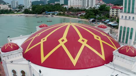 The-Tanjung-Bunga-floating-mosque-with-buildings-on-the-shore-and-boats-anchored-around-the-structure,-Aerial-drone-orbit-around-shot