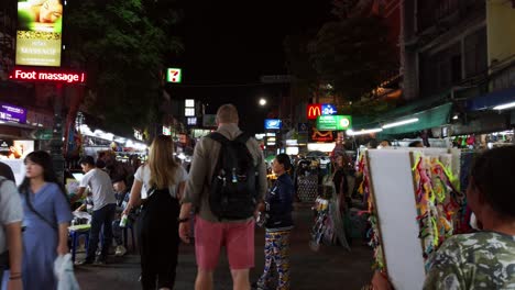 Escenas-De-Mano-De-Los-Turistas-Caminan-Por-La-Calle-Khao-San-En-La-Noche-Famosa-Que-Cada-Año-Turistas-De-Muchos-Países-Venían-A-Visitar-En-Bangkok,-Tailandia