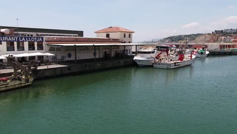 Aerial-View-of-Pier-in-Small-Spanish-Coastal-City-on-Mediterranean-Sea,-Tourist-Boats-and-Restaurant-in-Arenys-Del-Mar,-Spain