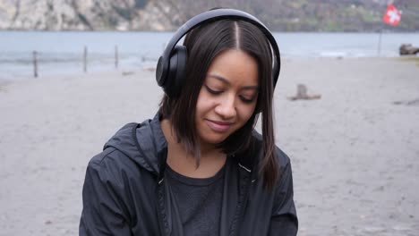 Happy-young-woman-stands-on-the-windy-shore-of-a-lake-listening-to-music-on-her-headphones---Tracking-shot