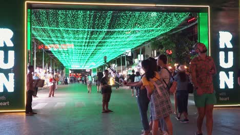 Medium-Exterior-Static-Shot-of-Three-Asian-Tourist-Girls-Taking-Selfies-As-Tourists-Walk-Pass-Amazed-by-the-green-Lights-on-Pub-Street