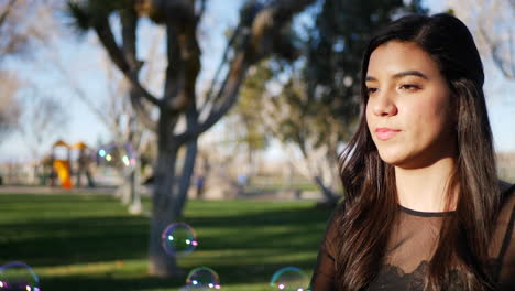 Attractive-hispanic-woman-blowing-bubbles-and-smiling-with-joy-and-happiness-as-she-has-fun-playing-in-the-sunny-park