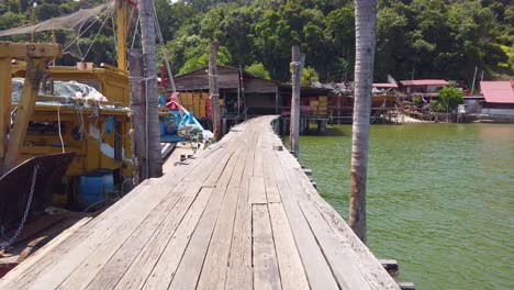 Eine-Schmale-Holzbrücke-Auf-Dem-Wasser-Mit-Schiffen,-Häusern-Und-Grünem-Wald-Im-Hintergrund-Auf-Der-Malaysischen-Insel-Pangkor