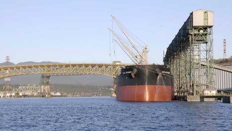 Ein-Frachtschiff-Ankert-Unter-Einer-Schönen-Gelben-Brücke-Mit-Industriegebäude-Auf-Der-Anderen-Seite-Der-Bucht-In-Vancouver,-Kanada-–-Weitwinkelaufnahme