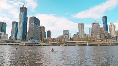 Eine-Gruppe-Von-Menschen,-Die-Im-Brisbane-CBD-River-In-Der-Nähe-Der-Southbank-Parklandschaft-Mit-Brisbane-Stadthintergrund-Kajak-Fahren