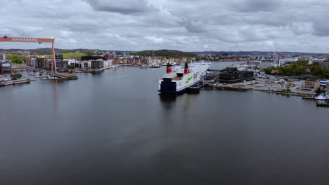 A-Huge-Ship-And-An-Overhead-Gantry-Crane-At-The-Industrial-Port-In-Gothenburg,-Sweden-On-A-Cloudy-Day---slow-ascending-drone-shot