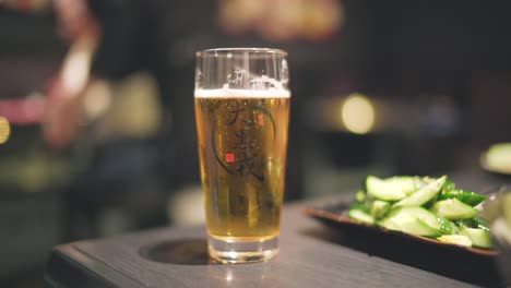 Glass-Of-Bubbling-Japanese-Beer-On-The-Wooden-Table-Inside-The-Restaurant-In-Kyoto,-Japan