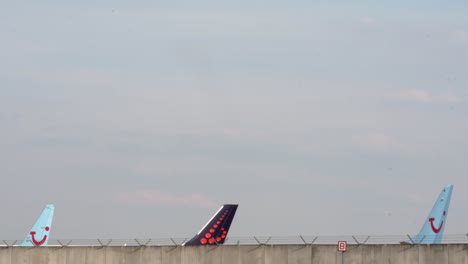 Aviones-De-Tui-Airways-Y-Brussels-Airlines-Elevándose-Por-Encima-De-Una-Pared-De-Alambre-De-Púas-Con-Sus-Aletas