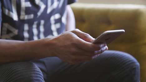 Close-up-of-a-man's-hands-using-an-iPhone-while-sitting-on-a-couch