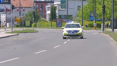 Coche-De-Policía-Con-Luces-De-Advertencia-Encendidas,-Dejando-Espacio-Para-Los-Competidores-De-Carreras-De-Bicicletas-Que-Vienen-Por-Las-Calles-De-La-Ciudad.