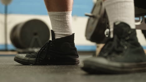 Man's-feet-while-sitting-on-benchpress-bench-in-between-sets-in-gym,-Slide-Right,-Slow-Motion