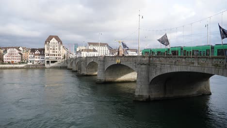 Establishing-shot,-Electric-tram-passing-a-bridge-over-the-Rhine-river-in-Basel,-Switzerland