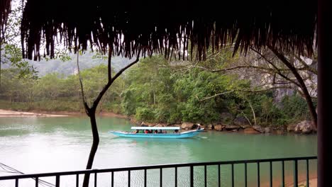 Barco-Turístico-De-Cuevas-Con-Personas-Con-Chalecos-Salvavidas-Acercándose-A-La-Entrada-De-La-Caverna-Vista-Desde-Una-Barandilla-Cercana,-Toma-Manual