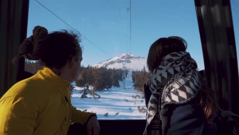 Young-couple-sits-in-gondola-ski-lift-watching-beautiful-snowy-landscape-outside