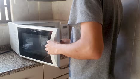 Young-man-warms-up-food-in-the-microwave-at-the-kitchen-counter