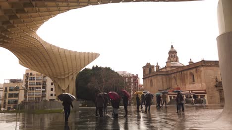 Menschen-Mit-Sonnenschirmen-Unter-Las-Setas-In-Sevilla,-Spanien-An-Einem-Regnerischen-Tag