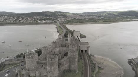 Medieval-landmark-historic-Conwy-castle-ruin-aerial-view-lowering-to-Welsh-seaside-landscape