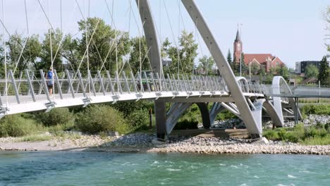 Landscaping-tractor,-cyclist-and-pedestrians-on-suspension-foot-bridge