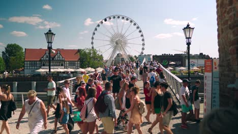 Gente-Caminando-Sobre-El-Puente-En-El-Centro-Con-La-Noria-De-Ferries-En-Segundo-Plano.