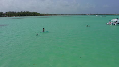 Circling-around-people-swimming-and-paddle-boarding-in-incredible-turquoise-ocean-water,-Playa-Jaunillo,-Dominican-Republic