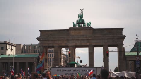 Protesters-in-slow-motion-on-a-COVID-19-corona-demonstration-against-wearing-face-masks-against-the-pandemic-in-Germany's-capital-Berlin,-holding-up-signs-and-approaching-the-Brandenburger-Tor