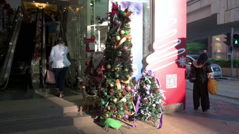 Fußgänger-Mit-Gesichtsmasken-Gehen-In-Hongkong-An-Einem-Geschäft-Für-Blumen-Und-Home-Deco-Produkte-Vorbei,-An-Dessen-Eingang-Ein-Weihnachtsbaum-Und-Ornamente-Ausgestellt-Sind
