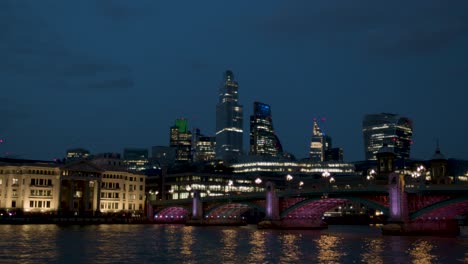 London-Thames-at-night,-bridge-lit-up-and-tall-buildings-in-the-background