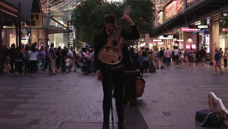 Los-Patreons-Caminan-Por-Las-Calles-Del-Centro-De-Sydney,-Australia,-Durante-Las-Vacaciones-De-Navidad-Mientras-Un-Hombre-Toca-La-Guitarra-Por-Dinero