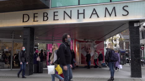 Ein-Von-Links-Nach-Rechts-Fahrender-Kamerawagen-Fährt-An-Einem-Baumstamm-Vorbei-Und-Zeigt-Menschen,-Die-Das-Kaufhaus-Debenhams-In-Der-Oxford-Street-Betreten-Und-Verlassen,-Während-Andere-Mit-Einkaufstüten-Vorbeigehen