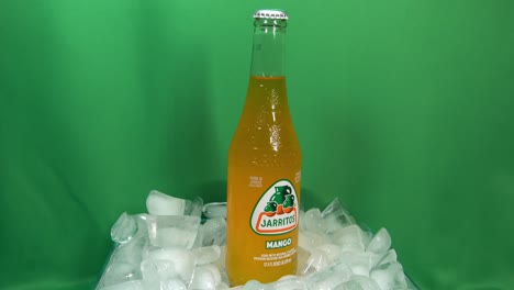 2-2-Botellas-De-Bebida-De-Mango-Carbonatado-Que-Giran-360-Grados-Sobre-Hielo-Apilado-Frente-A-Una-Pantalla-Verde