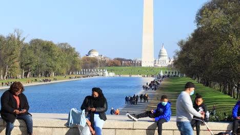 Two-mothers-and-their-children,-all-wearing-masks,-sit-on-a-bench-on-National-Mall-in-Washington,-D