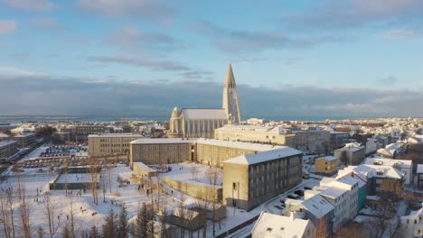 Drone-Aéreo-Sobre-La-Iglesia-Hallgrimskirkja-Cubierta-De-Nieve,-Catedral-A-La-Vista-En-Reykjavik,-Islandia