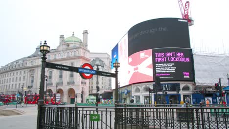 Cierre-En-Londres,-Autobuses-Rojos-Cámara-Lenta-Toma-De-Cardán-De-La-Estación-De-Metro-Piccadilly-Circus-Vacía-Frente-A-Carteles-LED-Que-Anuncian-Mensajes-Del-Virus-De-La-Corona