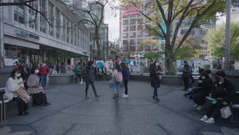 Hachiko-Memorial-Statue-At-Shibuya-City,-Tokyo,-Japan---People-In-Facemask-Walking-And-Sitting-On-Bench-Near-Hachiko-Statue-During-Pandemic