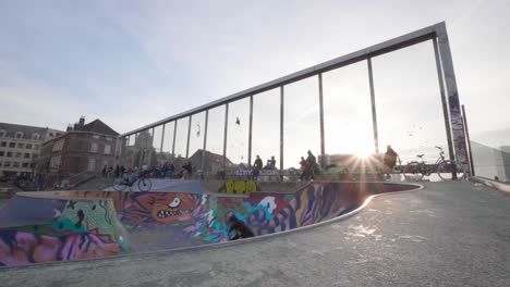 Drop-In-On-A-Skateboard-in-Concrete-Skate-Park-Pool-and-High-Jump-Air-Out-of-a-Bowl-with-the-sunset-background,-Slow-Motion