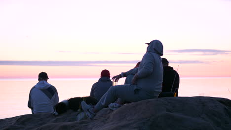 Eine-Gruppe-Männlicher-Freunde-Sitzt-Auf-Einer-Felsigen-Landschaft-Und-Beobachtet-Den-Orangefarbenen-Sonnenuntergang