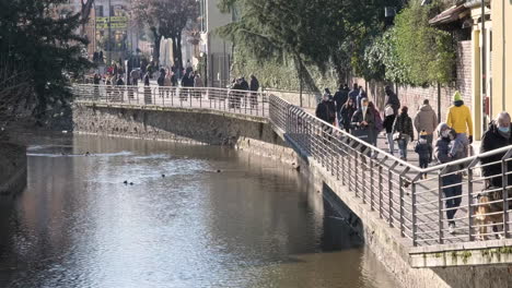 People-Walking-With-Face-Mask-Near-River-City-During-Covid-19-Pandemic-On-Winter-Sunny-Day-In-Monza,-Northern-Italy